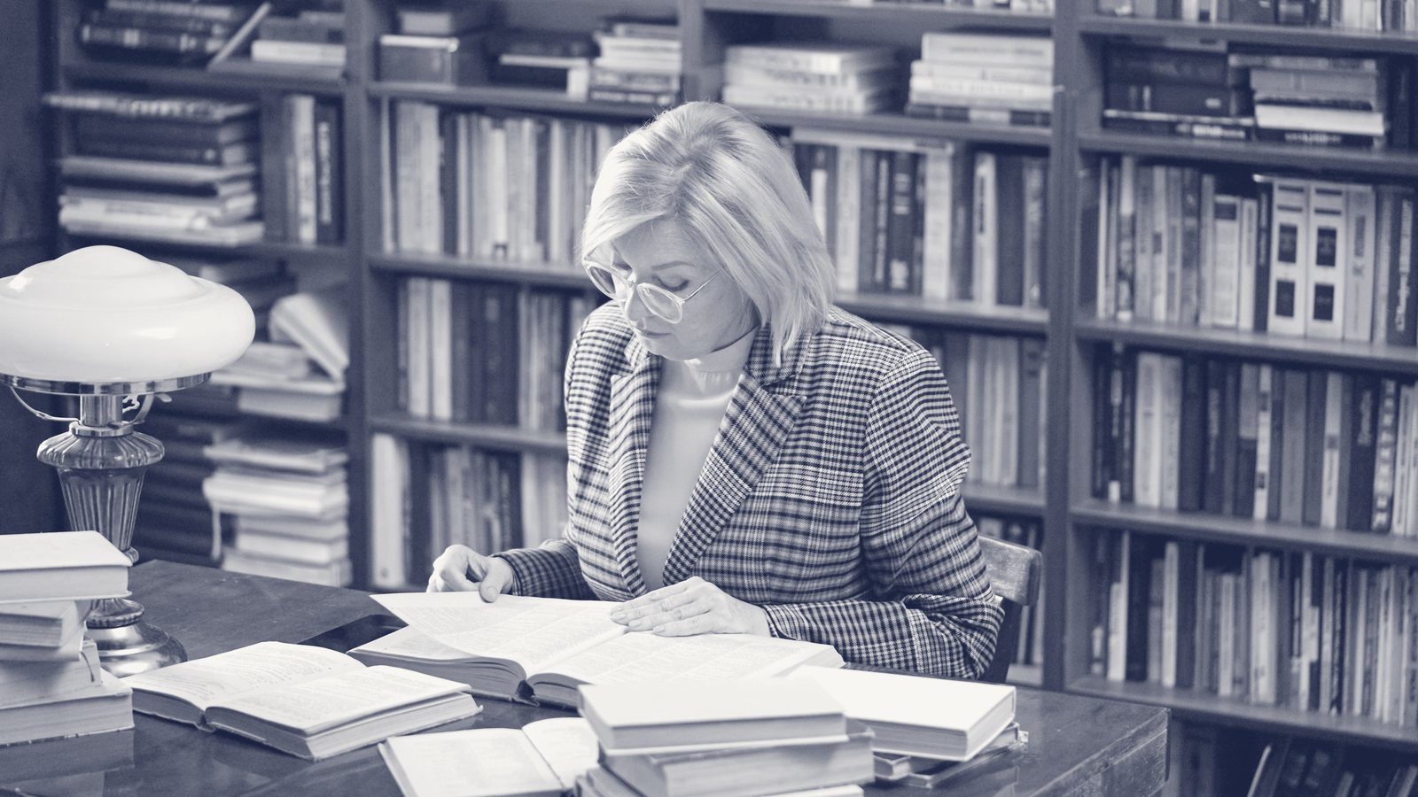 Retrato editorial en duotono de marca de una profesional senior leyendo entre libros.