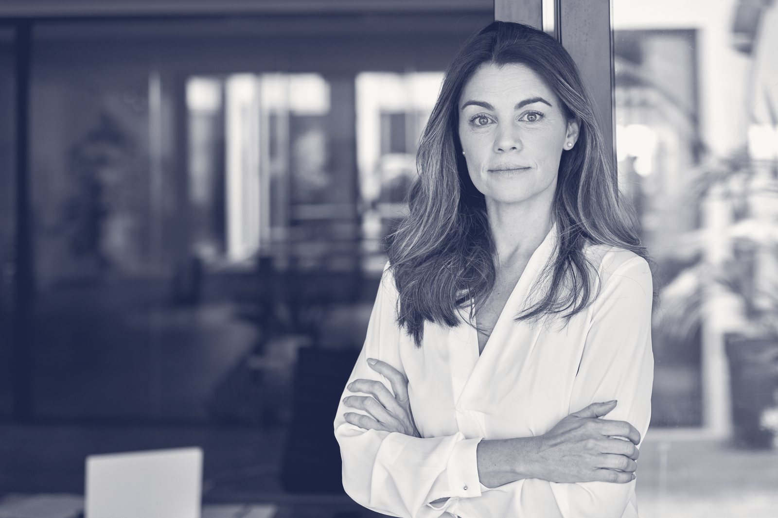 Retrato editorial en duotono de marca de una profesional senior de brazos cruzados, expresión serena y firme.