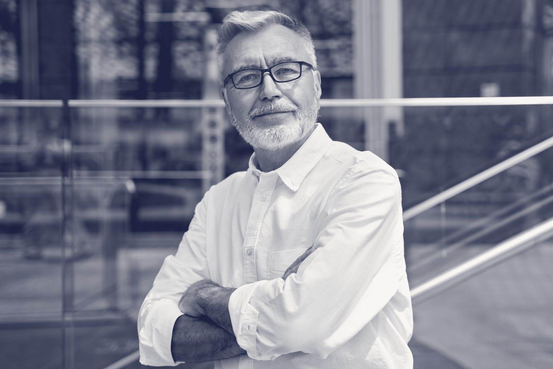Retrato editorial en duotono de marca de un profesional senior de brazos cruzados en un interior arquitectónico.